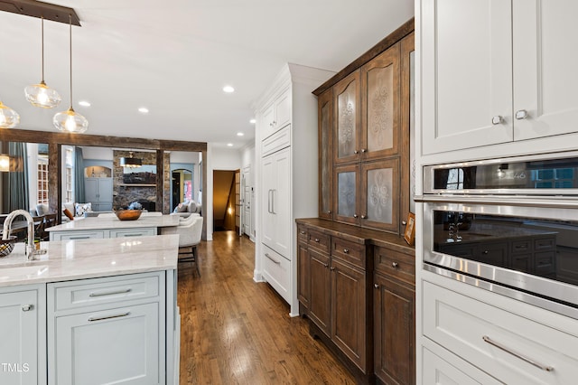 kitchen featuring light stone counters, open floor plan, dark wood-style flooring, oven, and a sink