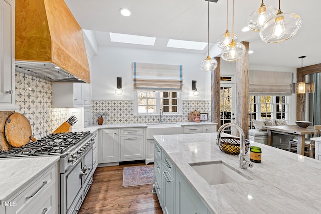 kitchen with premium range hood, gas range oven, a skylight, and a sink