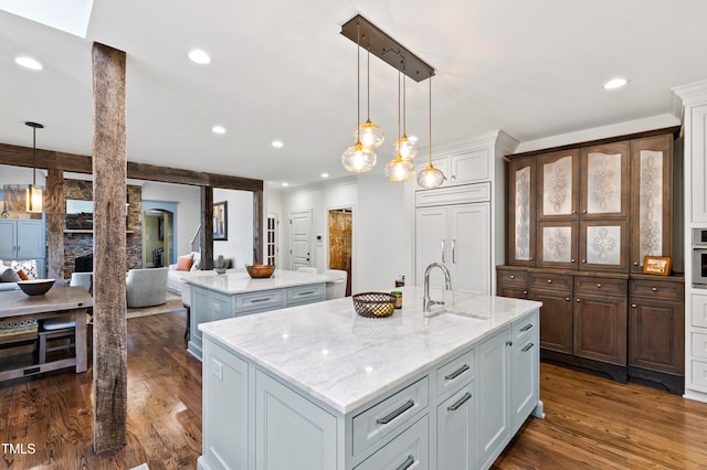 kitchen featuring dark wood-style floors, open floor plan, a kitchen island with sink, paneled refrigerator, and a sink