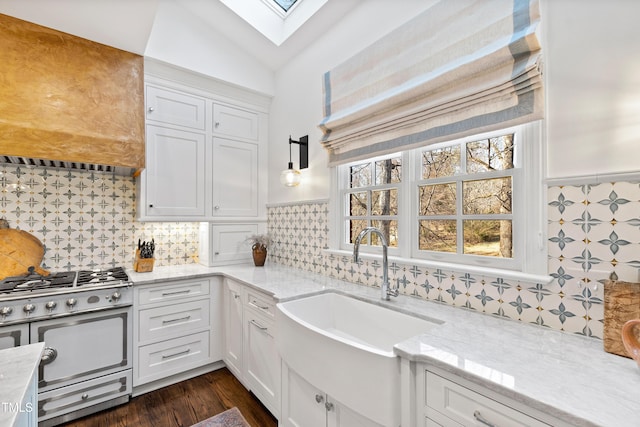 kitchen featuring wall chimney exhaust hood, gas stove, a sink, and white cabinetry