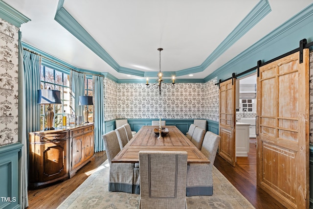 dining area featuring a barn door, a wainscoted wall, wood finished floors, a raised ceiling, and wallpapered walls