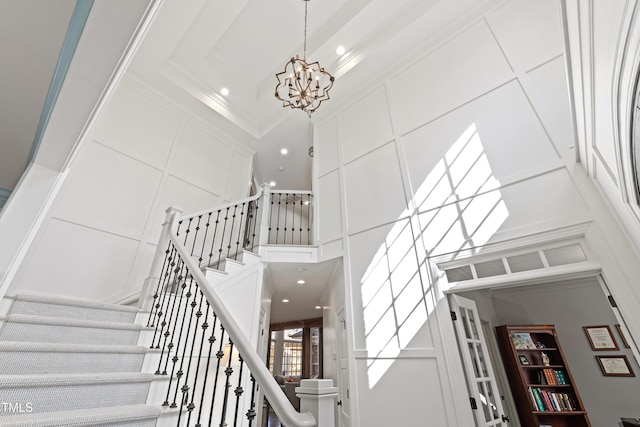 stairway with recessed lighting, a decorative wall, a towering ceiling, ornamental molding, and an inviting chandelier