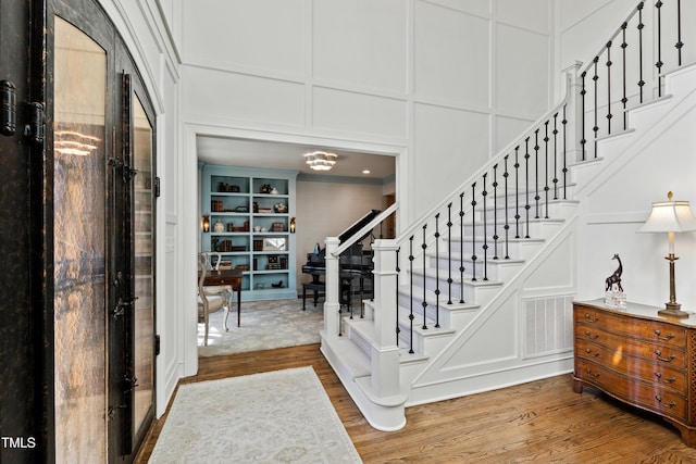 foyer entrance featuring visible vents, a decorative wall, stairway, and wood finished floors