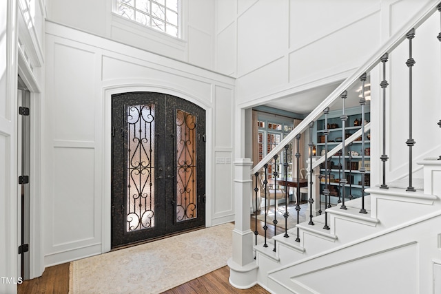 foyer entrance with a towering ceiling, stairway, a decorative wall, and wood finished floors