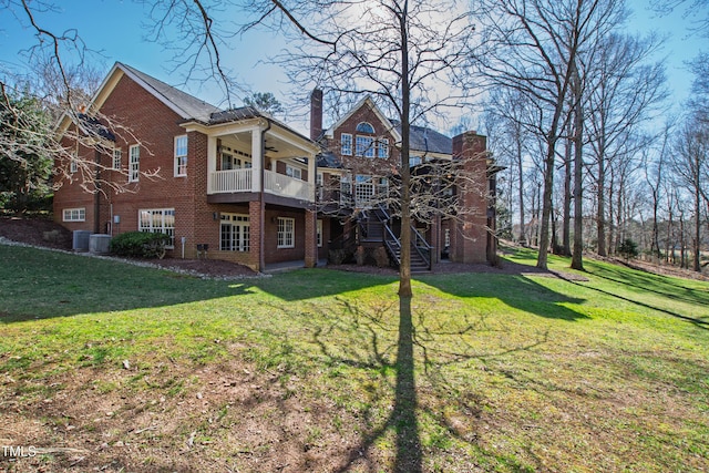 back of property with ceiling fan, stairway, a lawn, and brick siding