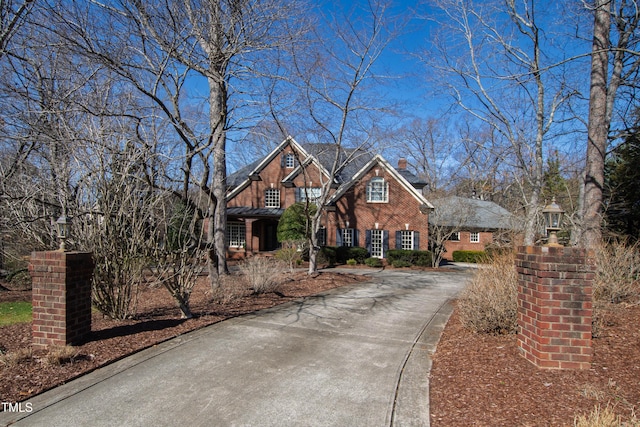 view of front of home with a chimney, concrete driveway, and brick siding