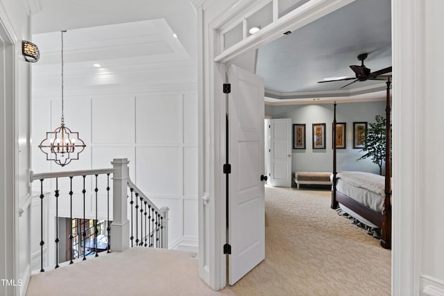 corridor featuring carpet, a tray ceiling, crown molding, an upstairs landing, and a decorative wall