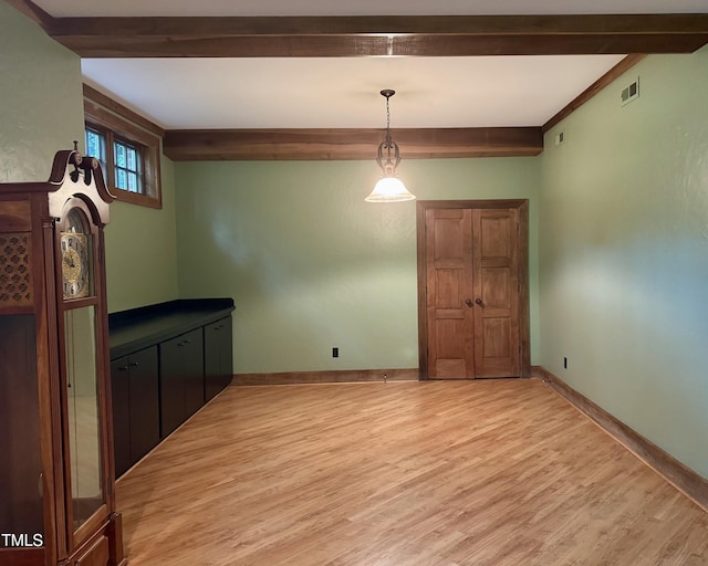 unfurnished dining area featuring baseboards, light wood-style floors, and beam ceiling