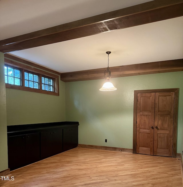 unfurnished dining area with light wood-style floors, baseboards, and beam ceiling
