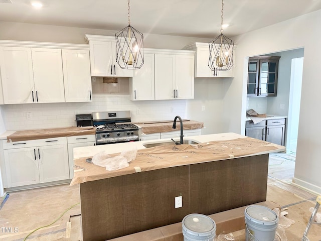 kitchen with decorative light fixtures, tasteful backsplash, stainless steel range with gas stovetop, a sink, and white cabinetry