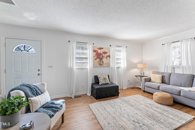 living area featuring light wood-type flooring, baseboards, and a textured ceiling