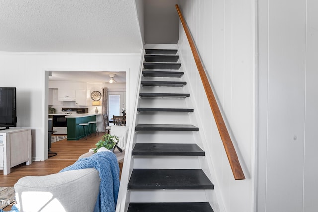 staircase with a textured ceiling, ornamental molding, and wood finished floors