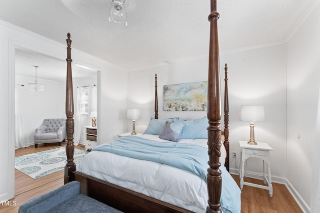 bedroom featuring a textured ceiling, ornamental molding, wood finished floors, and baseboards