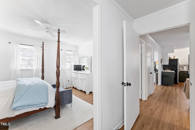 bedroom featuring a textured ceiling, a ceiling fan, ornamental molding, freestanding refrigerator, and light wood finished floors