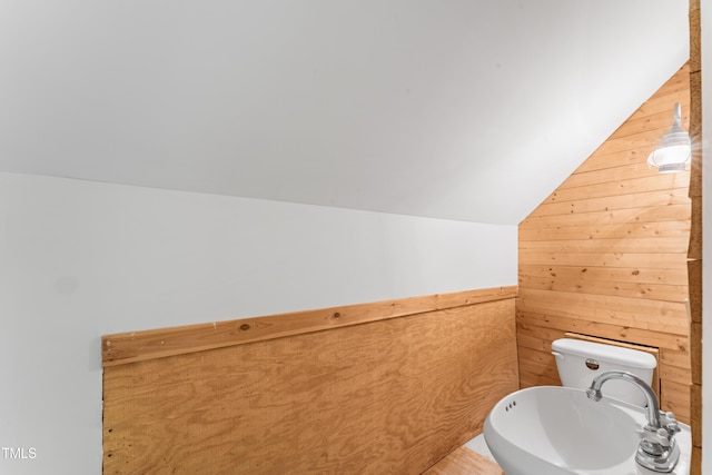 bathroom featuring vaulted ceiling, a sink, wooden walls, and toilet