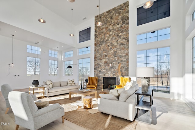 living area featuring light wood-style floors, a fireplace, a towering ceiling, and a healthy amount of sunlight