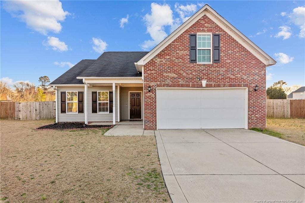 traditional-style home with a front yard, fence, concrete driveway, and brick siding