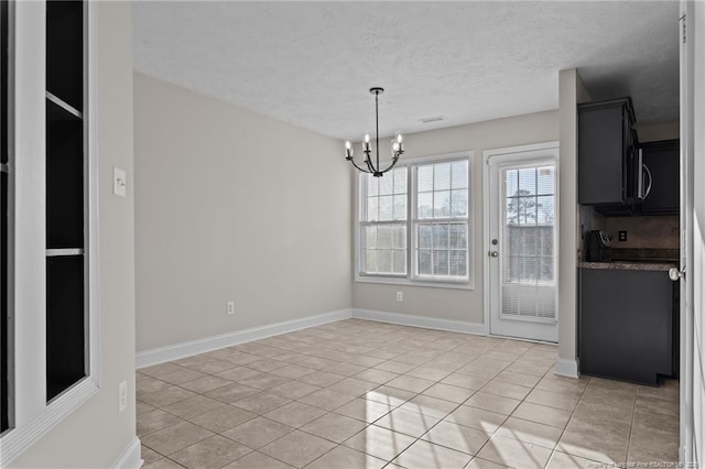 unfurnished dining area featuring a notable chandelier, a textured ceiling, baseboards, and light tile patterned floors