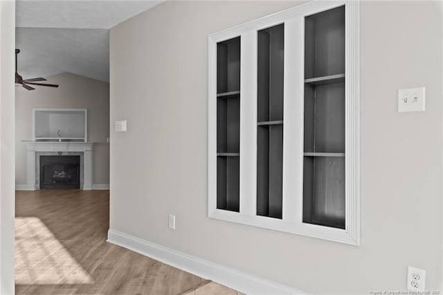 unfurnished living room featuring baseboards, a ceiling fan, lofted ceiling, wood finished floors, and a fireplace