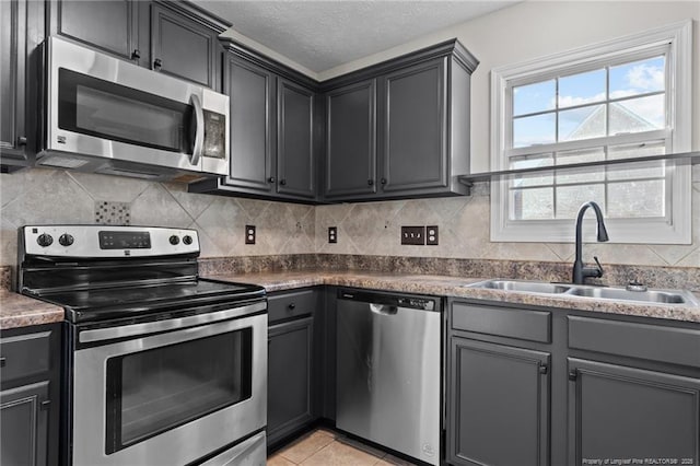 kitchen with tasteful backsplash, appliances with stainless steel finishes, light tile patterned flooring, a sink, and a textured ceiling