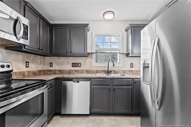 kitchen with light tile patterned floors, a textured ceiling, stainless steel appliances, a sink, and decorative backsplash