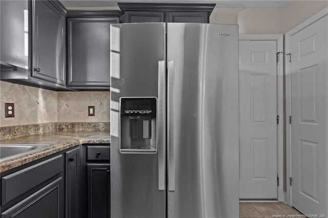 kitchen featuring a sink, stainless steel refrigerator with ice dispenser, decorative backsplash, and light tile patterned floors