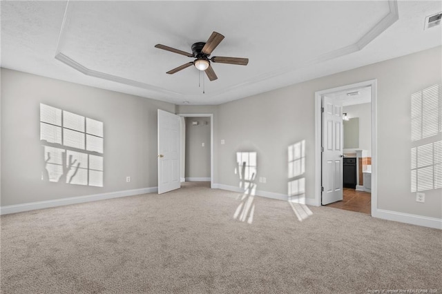 unfurnished bedroom featuring baseboards, a raised ceiling, connected bathroom, and light colored carpet