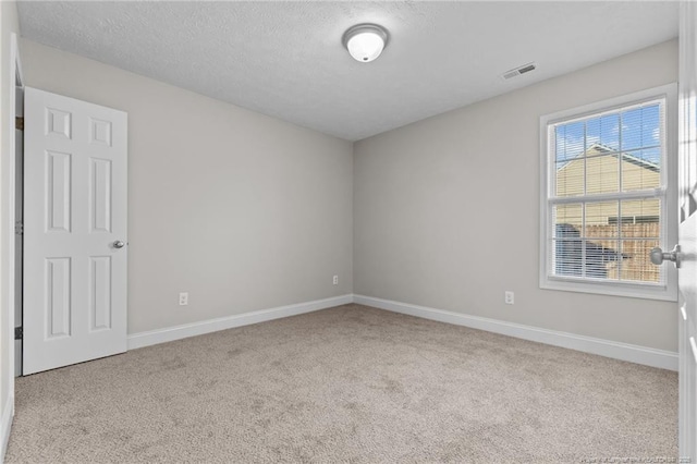 empty room with light colored carpet, visible vents, a textured ceiling, and baseboards