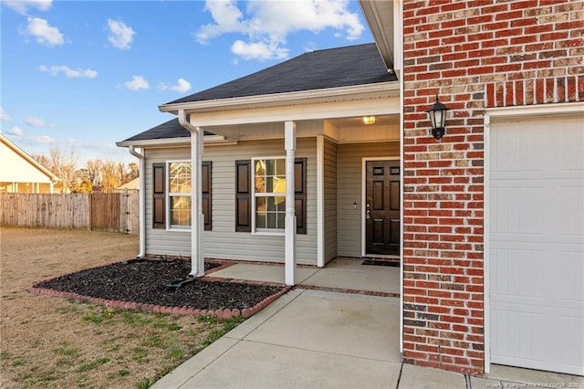 doorway to property featuring a garage, brick siding, a shingled roof, and fence