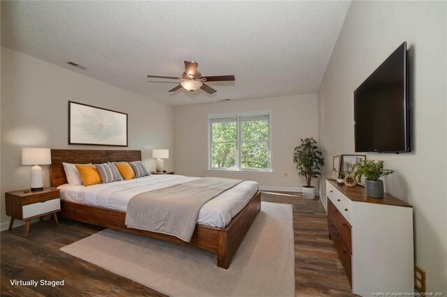 bedroom with dark wood-style flooring, a textured ceiling, visible vents, baseboards, and ceiling fan