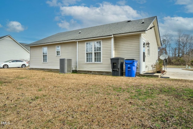 rear view of house featuring a shingled roof, a lawn, and central AC