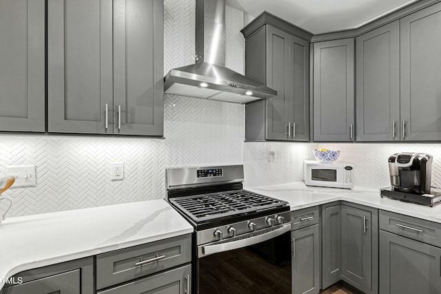 kitchen featuring gas stove, gray cabinets, wall chimney exhaust hood, and white microwave