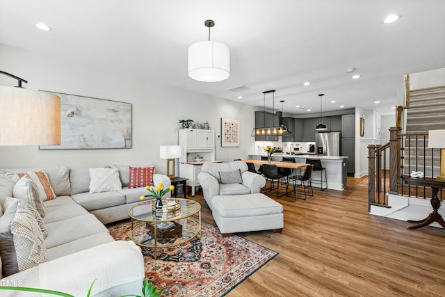 living room featuring light wood-type flooring, recessed lighting, and stairs