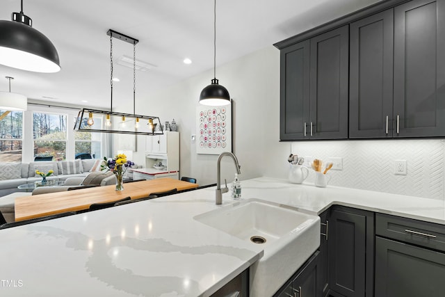 kitchen featuring decorative light fixtures, decorative backsplash, open floor plan, a sink, and light stone countertops