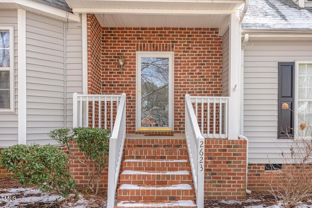 snow covered property entrance featuring crawl space and brick siding