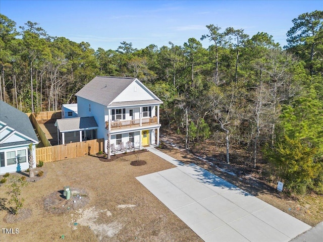 view of front of home with driveway, a balcony, a forest view, fence, and a porch