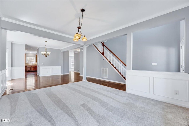 carpeted empty room with visible vents, stairs, ornamental molding, a notable chandelier, and a decorative wall