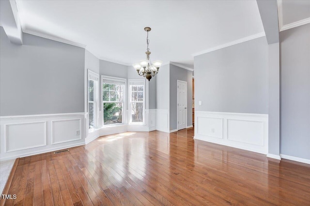 unfurnished dining area featuring visible vents, a wainscoted wall, ornamental molding, wood-type flooring, and a chandelier