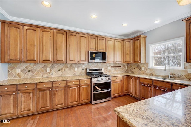 kitchen with light wood finished floors, light stone countertops, ornamental molding, stainless steel appliances, and a sink