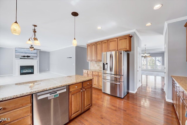 kitchen featuring backsplash, wood finished floors, stainless steel appliances, a large fireplace, and crown molding