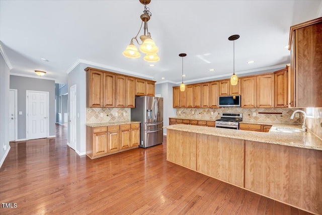 kitchen with a sink, light stone counters, wood finished floors, appliances with stainless steel finishes, and a peninsula