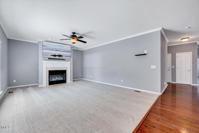 unfurnished living room with baseboards, a ceiling fan, a glass covered fireplace, and crown molding