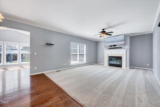 unfurnished living room featuring a glass covered fireplace, baseboards, and ornamental molding