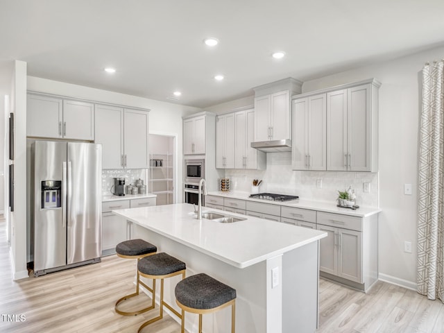 kitchen with a sink, stainless steel appliances, light wood-type flooring, and under cabinet range hood