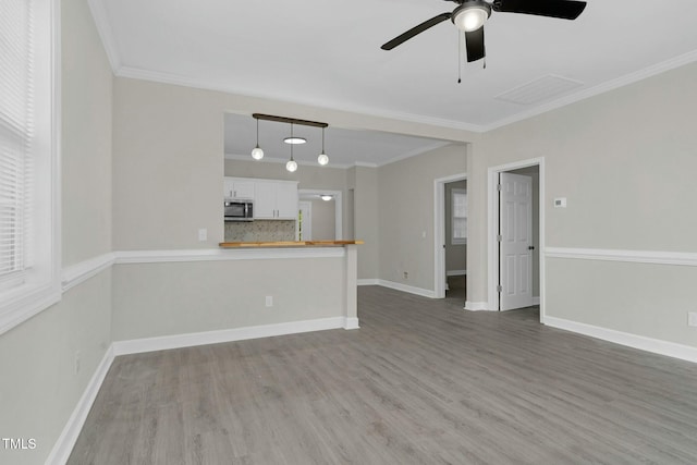 unfurnished living room with ornamental molding, visible vents, baseboards, and wood finished floors