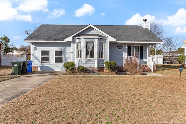 view of front facade featuring a chimney, a porch, a shingled roof, a front yard, and fence