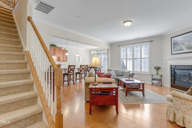 living area with light wood-type flooring, visible vents, and crown molding