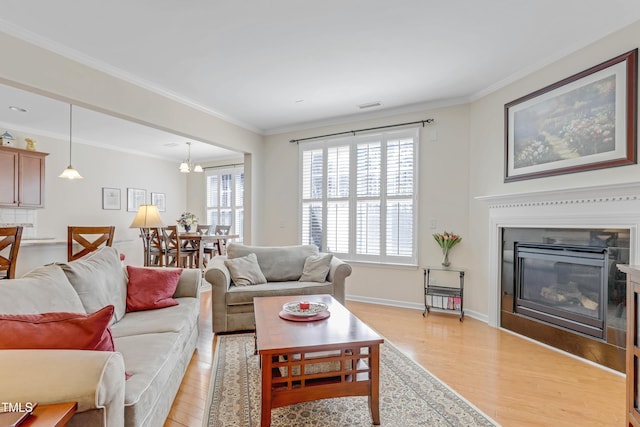 living area featuring ornamental molding, a glass covered fireplace, and light wood-style floors