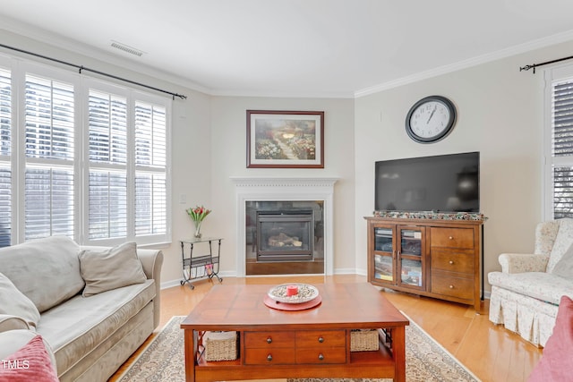 living area with wood finished floors, visible vents, baseboards, a glass covered fireplace, and crown molding