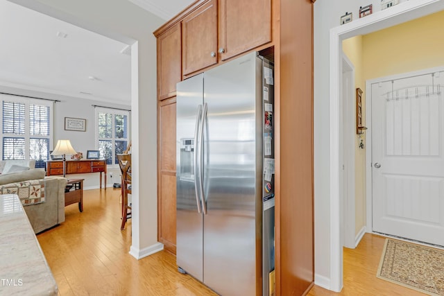 kitchen featuring light wood finished floors, stainless steel fridge, light countertops, and crown molding